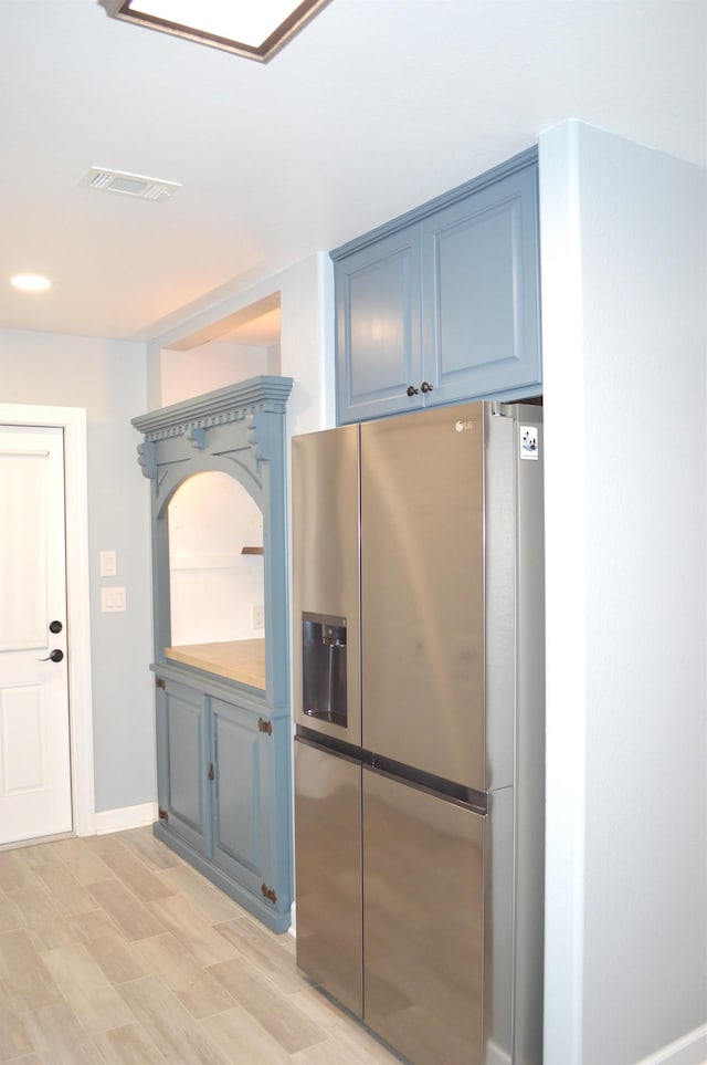 kitchen with stainless steel fridge, light wood-type flooring, and blue cabinets