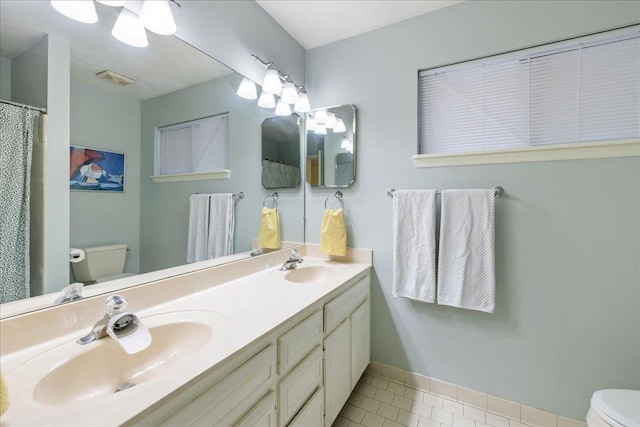 full bathroom featuring tile patterned flooring, a sink, toilet, and double vanity