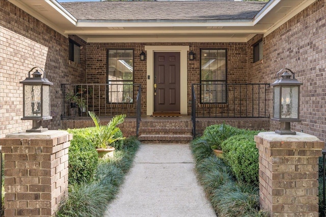 entrance to property with a shingled roof, covered porch, and brick siding