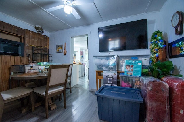 living room featuring wooden walls, hardwood / wood-style floors, ceiling fan, and ornamental molding