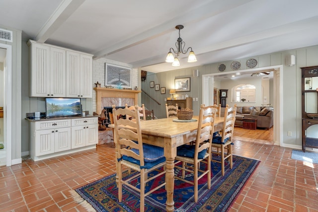 dining room featuring a notable chandelier, beam ceiling, and a fireplace