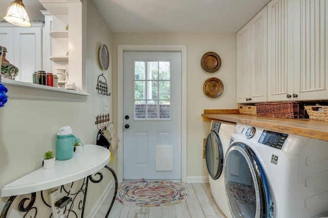 clothes washing area with washer and clothes dryer, light hardwood / wood-style floors, and cabinets