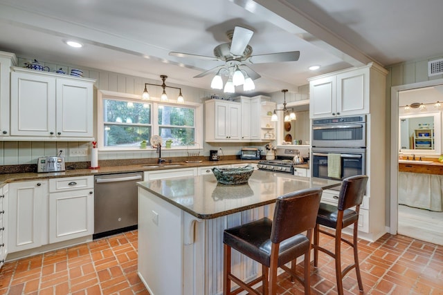 kitchen with stainless steel appliances, white cabinetry, a kitchen island, and decorative light fixtures