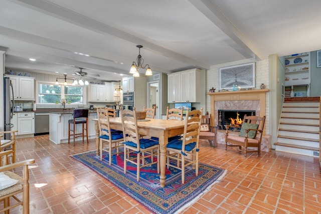 dining space featuring ceiling fan with notable chandelier, a fireplace, beam ceiling, and sink