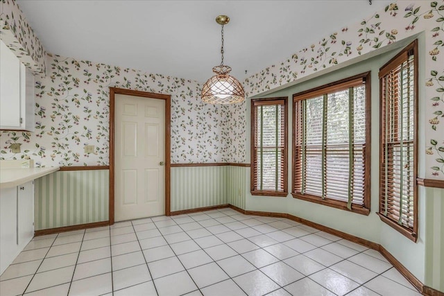 unfurnished dining area with a wainscoted wall, light tile patterned floors, and wallpapered walls