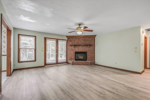 unfurnished living room with light wood-type flooring, a brick fireplace, and baseboards