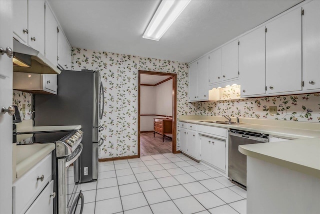 kitchen with under cabinet range hood, stainless steel appliances, a sink, light countertops, and wallpapered walls