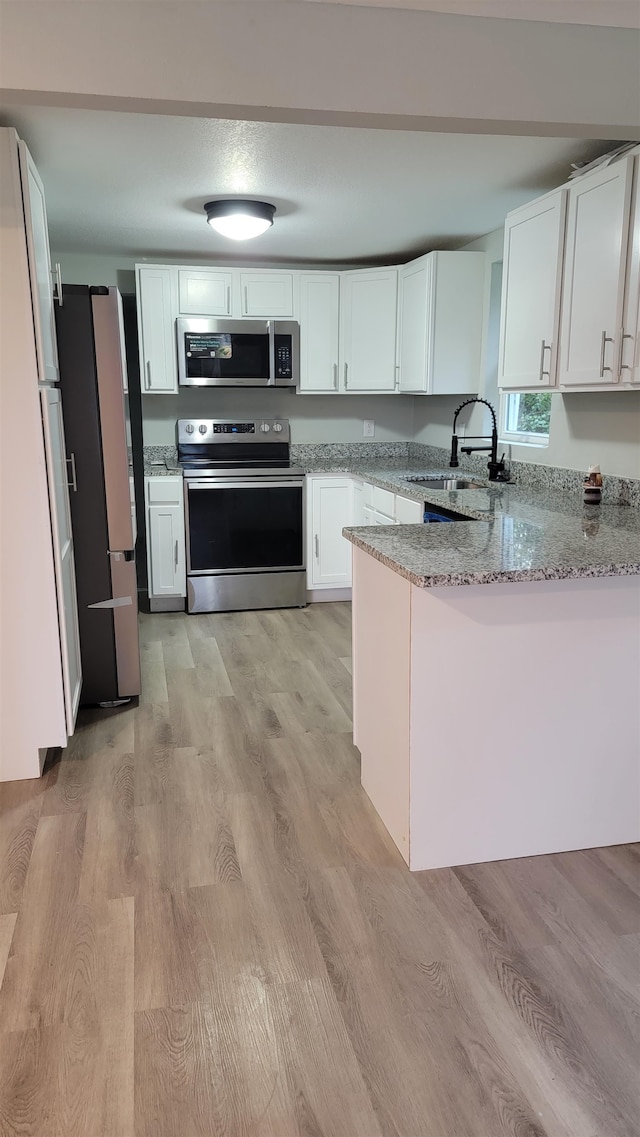 kitchen featuring light stone countertops, sink, light hardwood / wood-style flooring, and appliances with stainless steel finishes