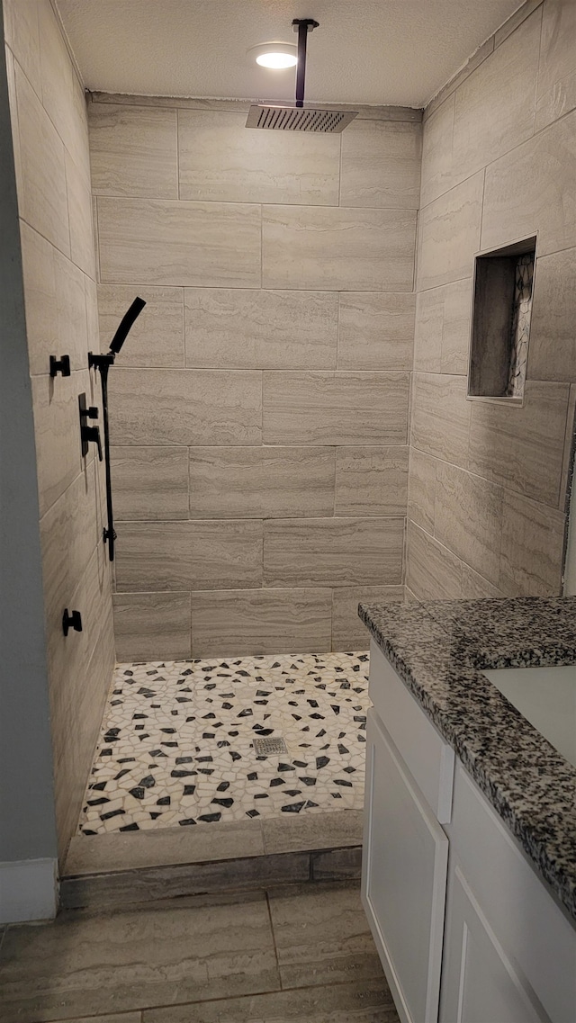 bathroom with tiled shower, a textured ceiling, and vanity