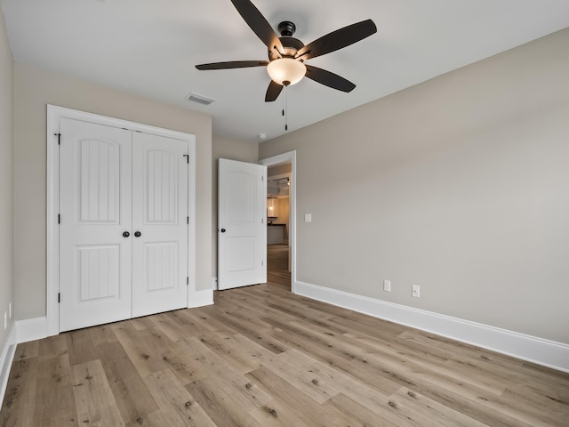 unfurnished bedroom with a closet, ceiling fan, visible vents, baseboards, and wood finished floors