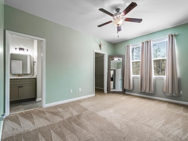 unfurnished bedroom featuring a sink, carpet flooring, ensuite bath, baseboards, and a spacious closet