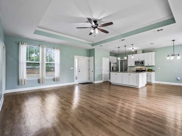unfurnished living room with dark wood finished floors, ceiling fan, baseboards, visible vents, and a tray ceiling