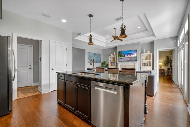 3260 Coneflower Dr, Tallahassee, FL 32311 - kitchen featuring stainless steel appliances, a sink, a tray ceiling, dark wood-style flooring, and dark stone counters