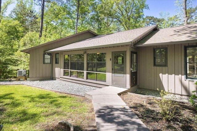 view of exterior entry featuring a yard, board and batten siding, and a shingled roof