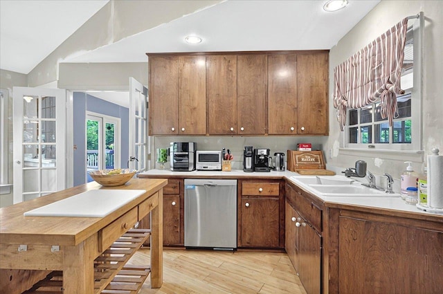 kitchen with dishwasher, a sink, a wealth of natural light, light wood-style flooring, and lofted ceiling