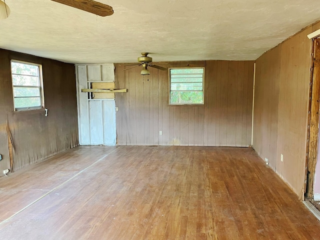 empty room with wood-type flooring, a wealth of natural light, ceiling fan, and wood walls