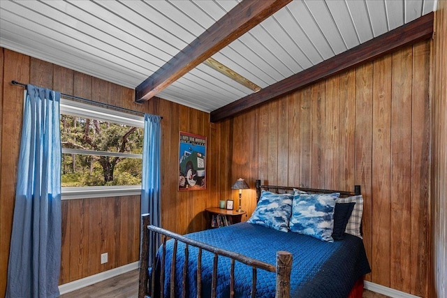 bedroom featuring beam ceiling, wooden walls, and hardwood / wood-style floors