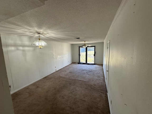 spare room featuring wood walls, a chandelier, a textured ceiling, ornamental molding, and carpet floors