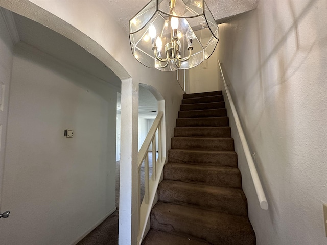 staircase featuring carpet floors, a textured ceiling, and a chandelier