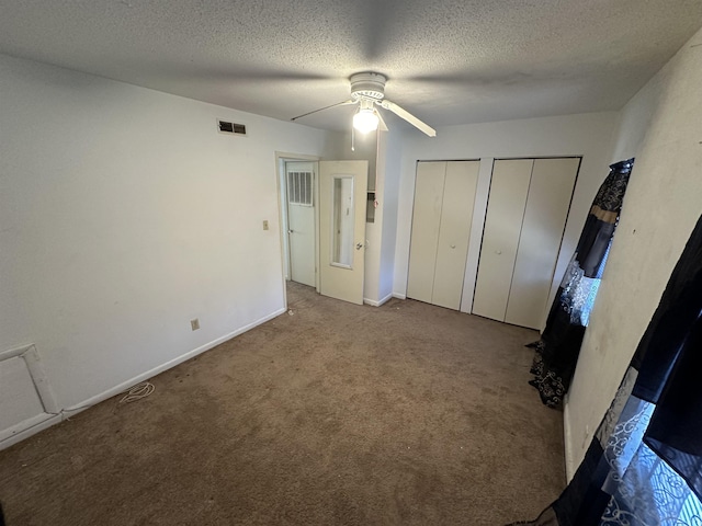 unfurnished bedroom with carpet flooring, two closets, a textured ceiling, and ceiling fan