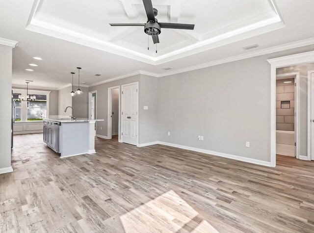 unfurnished living room with ceiling fan with notable chandelier, light wood-type flooring, crown molding, and a tray ceiling