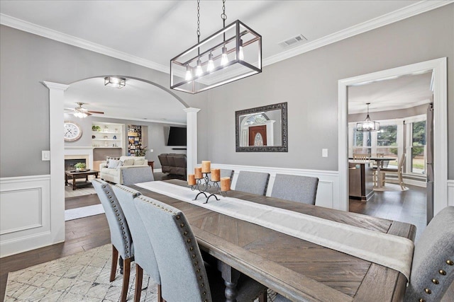 dining space featuring ceiling fan with notable chandelier, built in features, decorative columns, hardwood / wood-style flooring, and ornamental molding