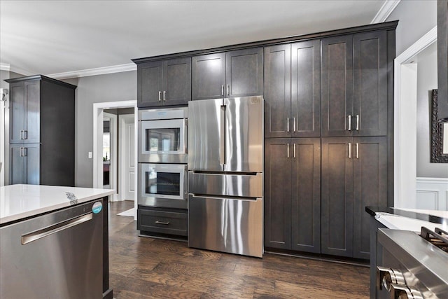 kitchen featuring dark brown cabinetry, ornamental molding, dark hardwood / wood-style floors, and appliances with stainless steel finishes