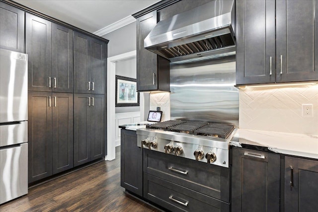 kitchen with backsplash, ornamental molding, stainless steel appliances, dark wood-type flooring, and wall chimney exhaust hood