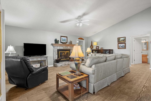 living room featuring vaulted ceiling, a textured ceiling, a fireplace, and ceiling fan