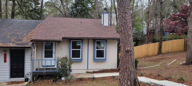 view of front of property featuring roof with shingles, fence, and a chimney