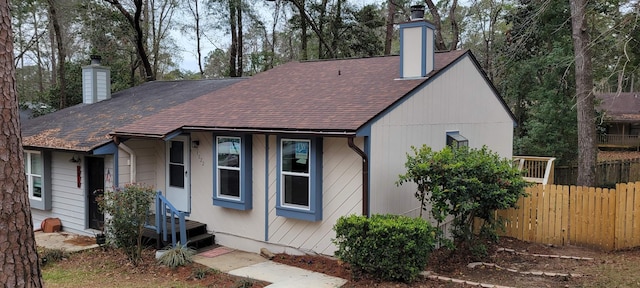 view of front of property featuring a shingled roof, fence, and a chimney