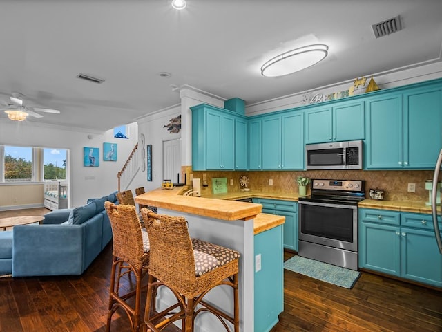 kitchen with wooden counters, blue cabinets, crown molding, dark hardwood / wood-style floors, and stainless steel appliances