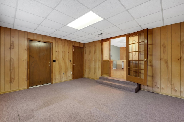 unfurnished room with a paneled ceiling, light carpet, and wood walls