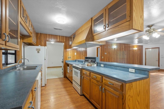 kitchen with light hardwood / wood-style floors, a textured ceiling, wooden walls, sink, and white appliances