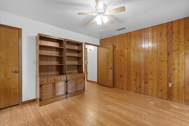 unfurnished bedroom with wood walls, light wood-type flooring, and ceiling fan