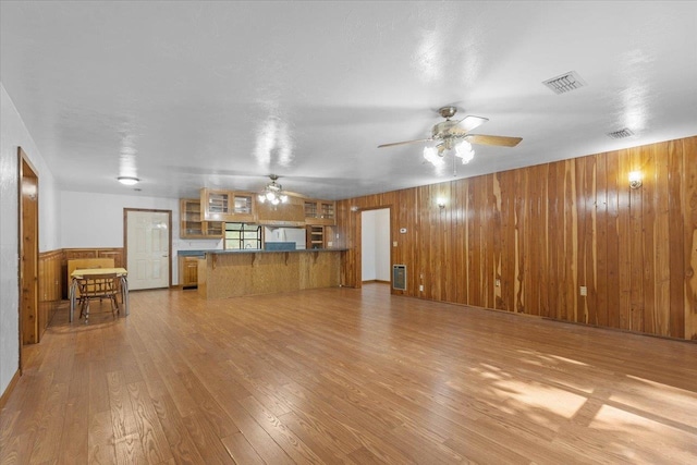 unfurnished living room featuring light hardwood / wood-style floors, wooden walls, and ceiling fan