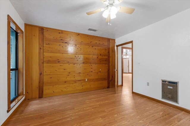 empty room with ceiling fan, wooden walls, and light hardwood / wood-style flooring