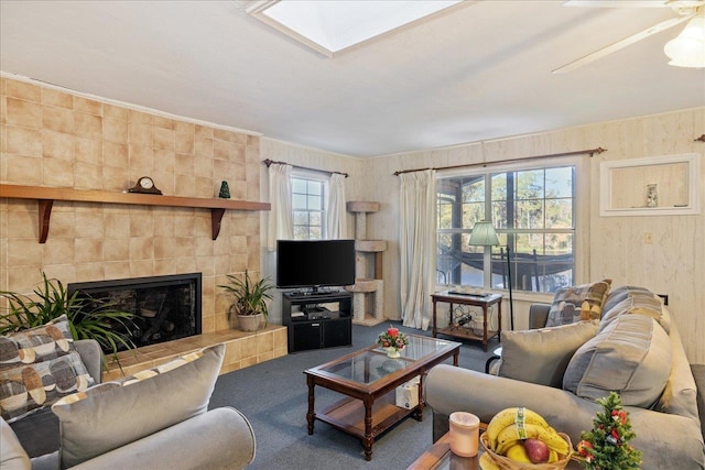 carpeted living room featuring a tile fireplace, a skylight, and ceiling fan