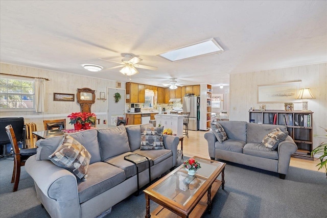 living room featuring a skylight, ceiling fan, light colored carpet, and a textured ceiling