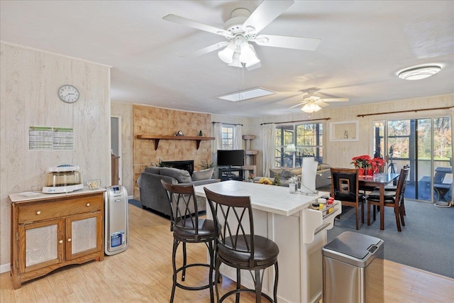 kitchen featuring a kitchen breakfast bar, light wood-type flooring, ceiling fan, a stone fireplace, and tile counters