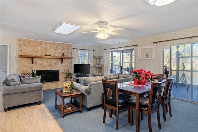 carpeted dining space with a skylight, ceiling fan, and a tiled fireplace