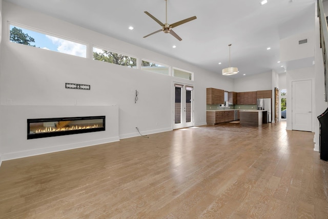 unfurnished living room featuring ceiling fan, a towering ceiling, and light wood-type flooring