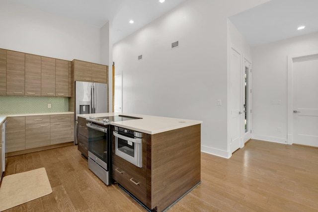 kitchen featuring decorative backsplash, appliances with stainless steel finishes, light hardwood / wood-style flooring, a high ceiling, and a center island