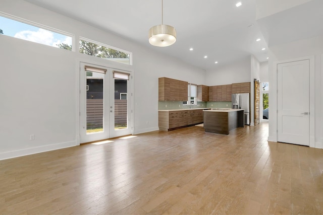 kitchen featuring stainless steel refrigerator with ice dispenser, pendant lighting, a high ceiling, a center island, and light hardwood / wood-style floors