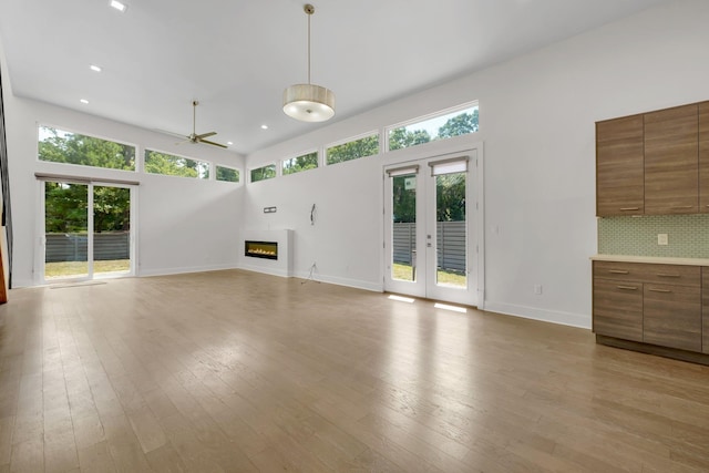 unfurnished living room featuring french doors, light hardwood / wood-style floors, ceiling fan, and a high ceiling