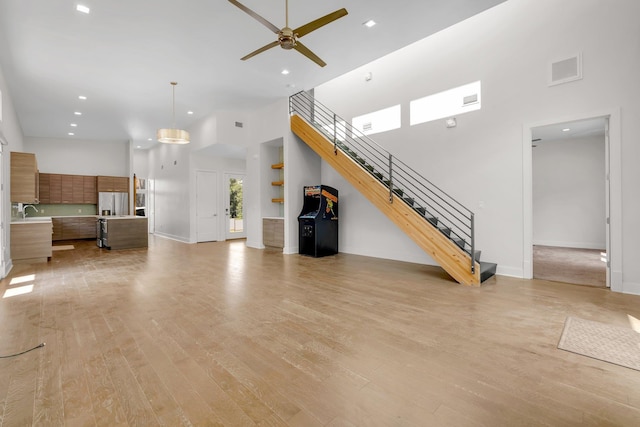 unfurnished living room featuring a towering ceiling, light hardwood / wood-style floors, and ceiling fan