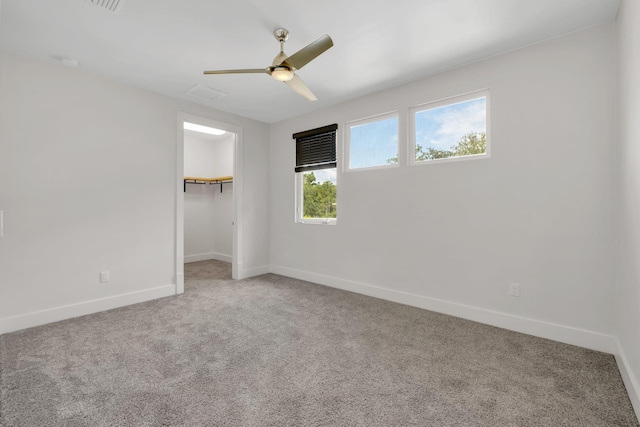 unfurnished bedroom with a walk in closet, a closet, ceiling fan, and carpet floors