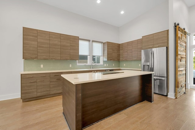 kitchen with decorative backsplash, stainless steel refrigerator with ice dispenser, a barn door, a high ceiling, and a kitchen island