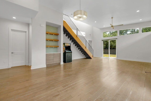 unfurnished living room featuring ceiling fan, light hardwood / wood-style flooring, and a towering ceiling