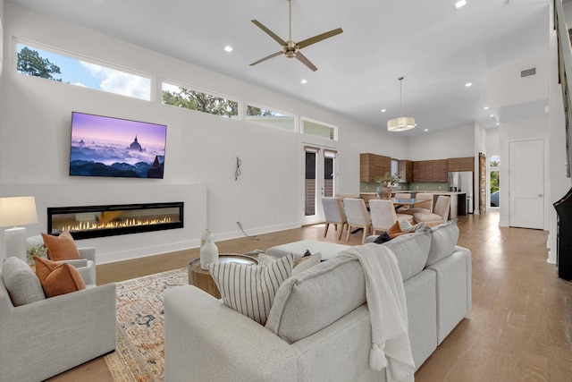 living room with ceiling fan, light wood-type flooring, and a towering ceiling